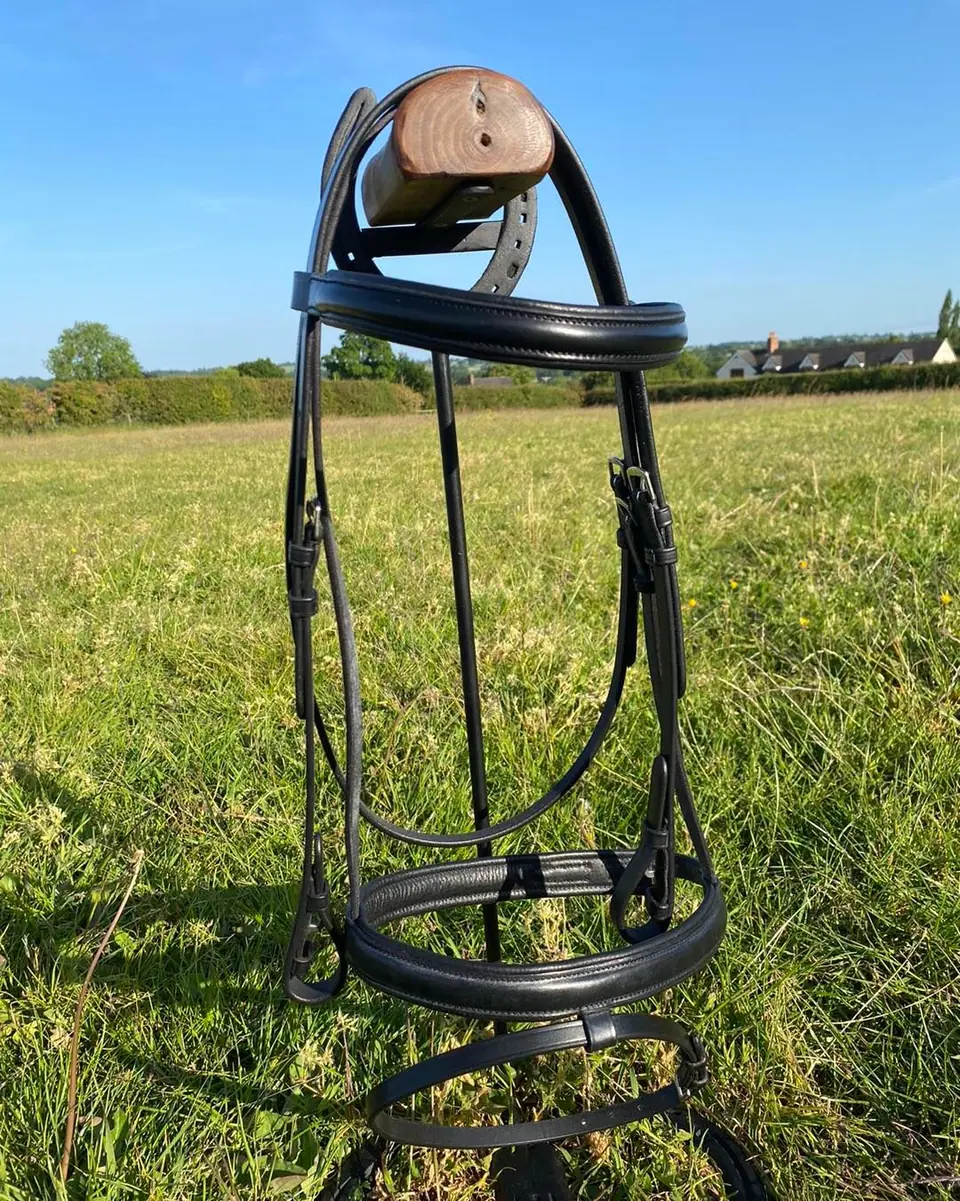 A padded black bridle on a stand in a field