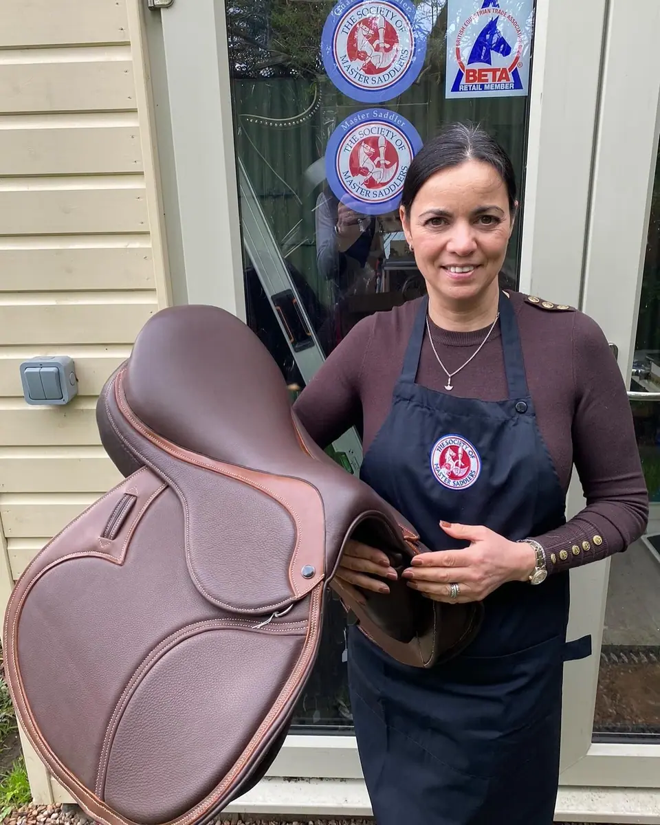 Kate in her workshop apron holding a new saddle