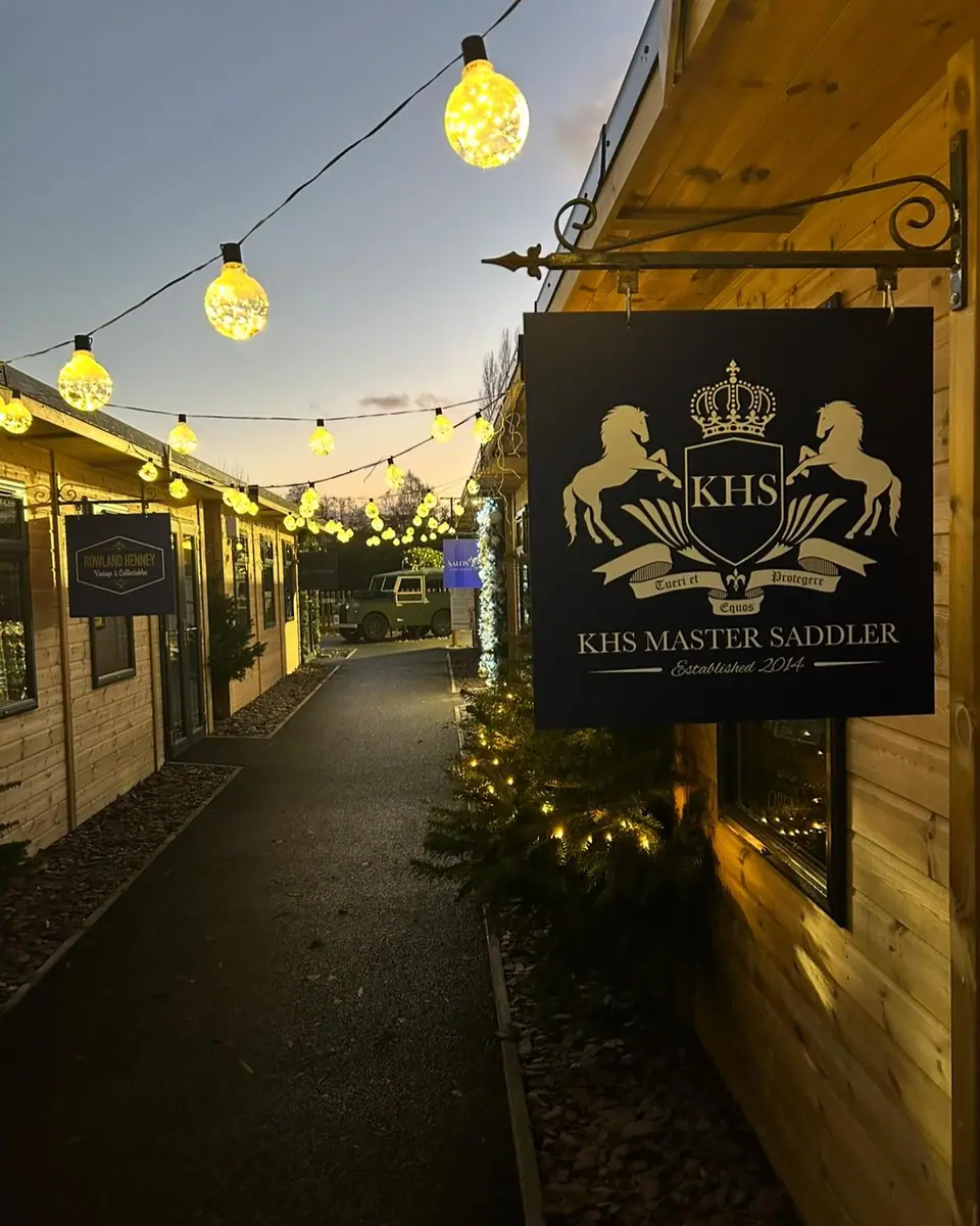 The KHS Master Saddler sign at dusk under festoon lights at Fletchers Garden Village